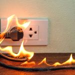 Close-up of a severely damaged electrical outlet showing burn marks and melted plastic on wall, demonstrating fire damage from delayed electrical repairs