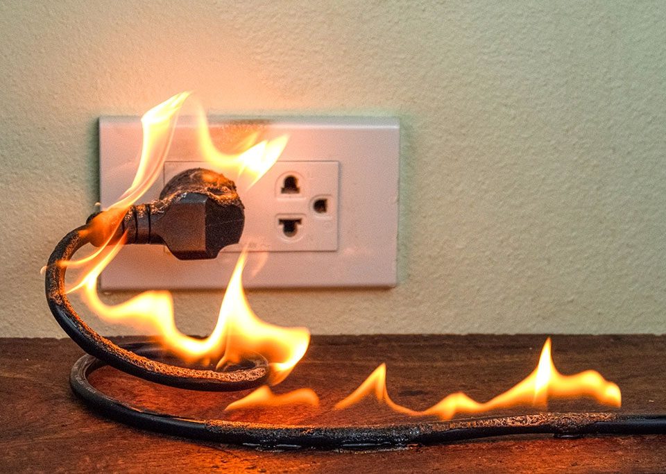 Close-up of a severely damaged electrical outlet showing burn marks and melted plastic on wall, demonstrating fire damage from delayed electrical repairs