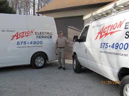 Bob bishop of action electric stands between two white vans labeled Action Electric Service with a phone number, parked outside a building on a sunny day.